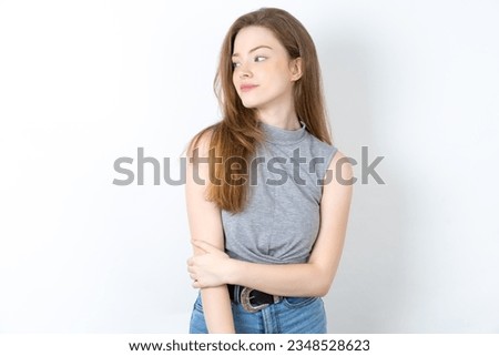 Pleased young beautiful blonde woman standing over blue studio background keeps hands crossed over chest looks happily aside