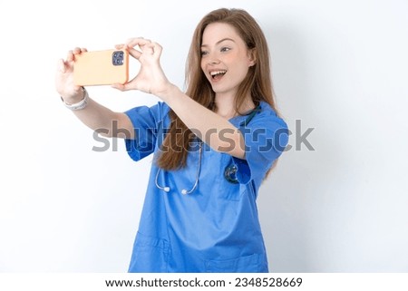 young beautiful doctor woman standing over white studio background taking a selfie to post it on social media or having a video call with friends. Royalty-Free Stock Photo #2348528669
