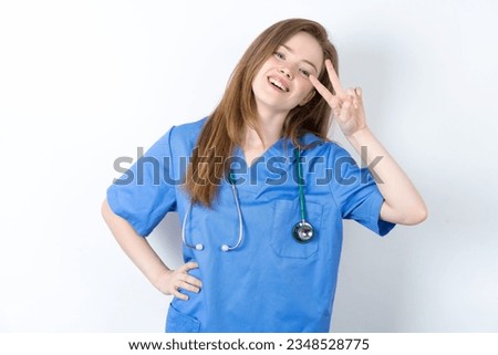 young beautiful doctor woman standing over white studio background Doing peace symbol with fingers over face, smiling cheerful showing victory