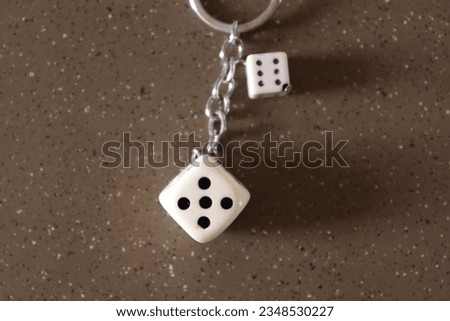 Two White Dice tied with chain and a ring on a Brown texture marble Surface 