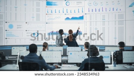 Back View Of Indian Data Analyst And Hispanic Manager Discussing Reports On Digital Screen in Monitoring Room. Male and Female Experts Talking, Employees Working On Computers In Consulting Company Royalty-Free Stock Photo #2348534963