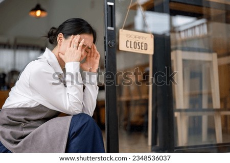 A crying and upset young Asian female coffee shop owner is hanging a close sign at the entrance door, feeling sad to close her business. Business close down