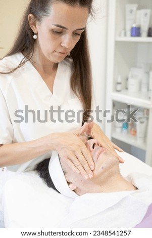 facial massage to a middle-aged man by a young esthetician, skin care concept . High quality photo