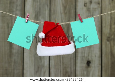 Blank green Christmas cards and red Santa Claus hat hanging from clothesline with antique wooden background
