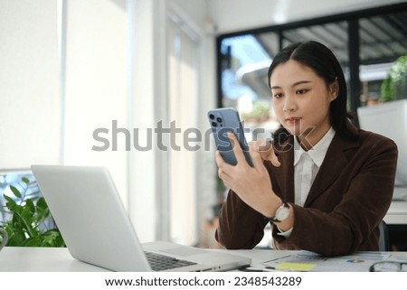 Image of female office worker sitting at desk and checking social media, texting message on smartphone..