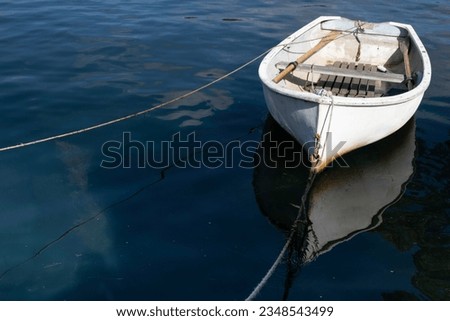 Small white fishing boat tied with a rope, floats in dark blue water. . Boat mirrored in water. Space for text or design Royalty-Free Stock Photo #2348543499