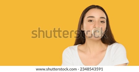 Beautiful young woman blowing bubble gum on yellow background Royalty-Free Stock Photo #2348543591