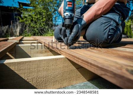 Deck construction, builder hand with electric screwdriver installing impregnated wooden boards Royalty-Free Stock Photo #2348548581