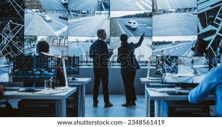 Two Diverse Male and Female Software Engineers Discuss Live Analysis Feed with City Road and Traffic Updates. Managers and Data Scientists Collaborate in a Modern Monitoring Office Royalty-Free Stock Photo #2348561419