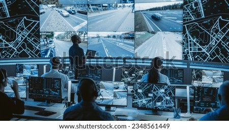 Male Software Engineer Working on Laptop Next to a Big Screen in a Modern Monitoring Office with Live CCTV Footage with Traffic Situation. Monitoring Room With Big Data Engineers Work on Computers Royalty-Free Stock Photo #2348561449