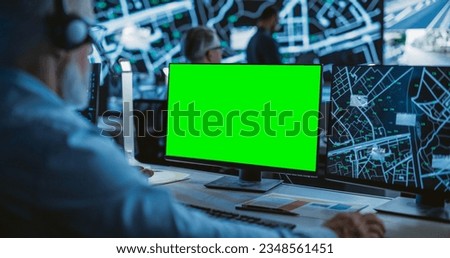 Middle Aged Surveillance Specialist Working on a Computer with Green Screen Mock Up Display. Manager Effectively Multitasking with Supporting Clients on a Phone Call and Computer Work