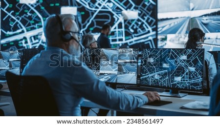 Technical Customer Support Specialist is Talking on a Headset while Working on a Computer in a Call Center Control Room Filled Display Screens with Monitoring Software. Over the Shoulder Footage