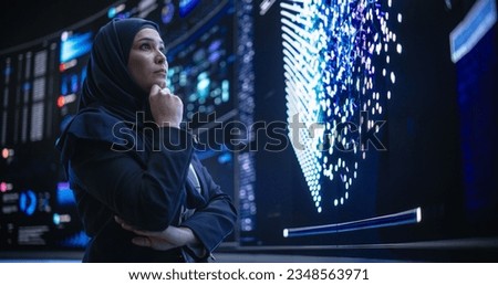 Portrait of a Smart Focused Middle Eastern Software Engineer Analyzing Neural Network Big Data on a Digital Screen. Young Arab Woman in Hijab Working in an Innovative Internet Service Company Royalty-Free Stock Photo #2348563971