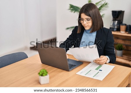 Young beautiful hispanic woman business worker using laptop reading document at office
