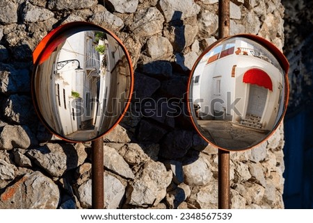 Two circular old traffic mirrors with red frames reflecting narrow streets in a village on Capri island, Italy. Holiday atmosphere on a sunny summer day in mediterranean surrounding.