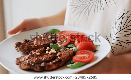 The girl holds in her hands a plate with vegetables and cooked, fragrant meat on a light background.
