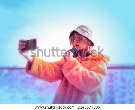 Young pretty woman social media influencer. Portrait of stylish good-looking Teenage girl blogger, in a yellow fur coat, taking selfie, hold mobile phone.