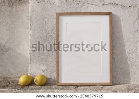 Minimal empty vertical wooden frame picture mock up against white old textured white wall in sunlight. Fresh yellow lemons fruit. Summer background with light, shadows. Mediterranean design. 