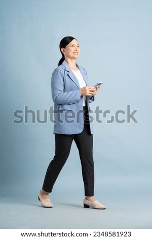 full body photo of a middle aged businesswoman using a smartphone posing on a blue background Royalty-Free Stock Photo #2348581923
