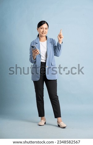 full body photo of a middle aged businesswoman using a smartphone posing on a blue background Royalty-Free Stock Photo #2348582567