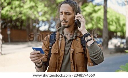 Young hispanic man tourist talking on smartphone holding credit card at park