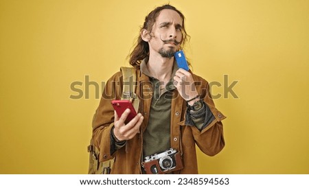Young hispanic man tourist shopping with credit card and smartphone thinking over isolated yellow background