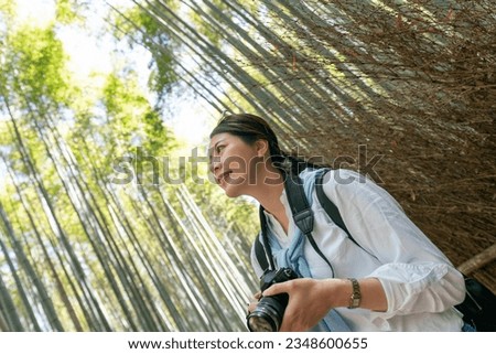 dutch angle shot of happy asian Japanese woman tourist looking up at towering bamboos while visiting Arashiyama Bamboo Grove in Kyoto japan on a sunny day Royalty-Free Stock Photo #2348600655