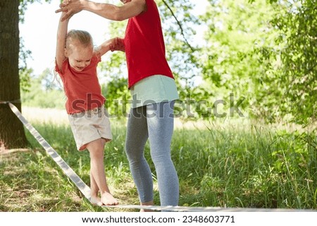 Playful girl enjoying while doing slacklining with mother in garden Royalty-Free Stock Photo #2348603771