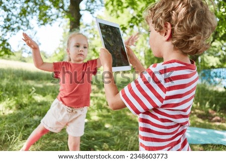Brother clicking picture of sister through digital tablet in garden