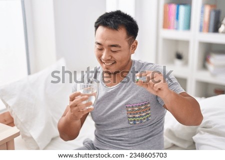 Young chinese man taking pill drinking water sitting on bed at bedroom Royalty-Free Stock Photo #2348605703