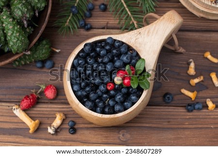 Collected edible orange chanterelle mushrooms on a wooden plate with cranberries, blueberries and strawberries. Wooden plate with mushrooms, green spruce branches and fir cones
