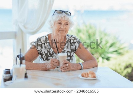 Portrait of attractive senior woman sitting in a summer outdoor cafe and drinking coffee