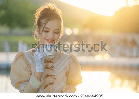 Beautiful Asian girl in the Victorian or Edwardian era dressed relaxed and having a happy afternoon tea party in nature on the river bank, enjoying picnicking, reading books, and sipping tea.