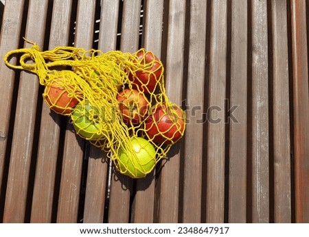 Green and red apples in an eco-friendly yellow bag on a background. Minimalistic horizontal photo