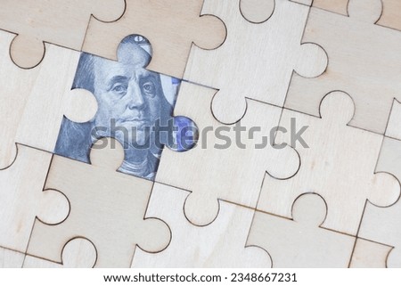 The wooden jigsaw has a gap with dollar bills underneath.