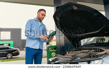 The man is standing in front of the raised hood, checking and changing the oil at the gas station Royalty-Free Stock Photo #2348669469