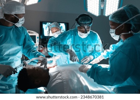 Diverse surgeons wearing surgical gowns operating on patient in operating theatre at hospital. Hospital, surgery, hygiene, teamwork, medicine, healthcare and work, unaltered. Royalty-Free Stock Photo #2348670381