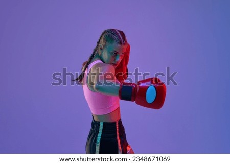 Sportive teen girl, MMA athlete in uniform and boxing gloves, training against purple background in neon lights. Concept of mixed martial arts, sport, hobby, competition, athleticism, strength, ad
