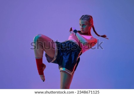 Leg kick. Sportive teen girl, mma fighter athlete in motion, training, fighting against purple background in neon lights. Concept of mixed martial arts, sport, hobby, competition, strength, ad Royalty-Free Stock Photo #2348671125