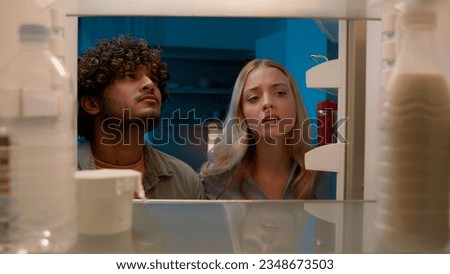 Point of view POV inside refrigerator Caucasian girl woman girlfriend wife and Arabian man Indian guy boyfriend husband multiracial couple at night evening open empty fridge at kitchen unhappy sad Royalty-Free Stock Photo #2348673503