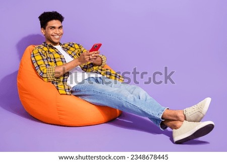 Full body portrait of positive funky person sit comfort bag use smart phone chatting isolated on purple color background Royalty-Free Stock Photo #2348678445