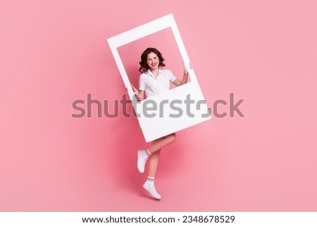 Full length photo of cute pretty lady wear white blouse jumping high holding paper frame isolated pink color background