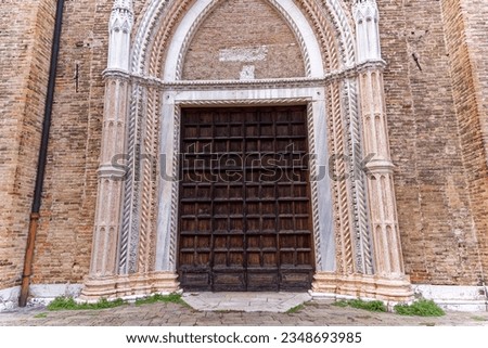 Close-up of brick wall and entrance with wooden gate of church at the old town of Venice on a sunny summer day. Photo taken August 6th, 2023, Venice, Italy.
