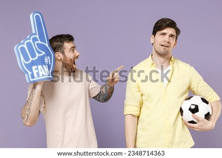 Two young loser sad men friends together wear casual t-shirt fan foam glove finger mocking joke laughing bullying point index finger on buddy isolated on purple background studio. Tattoo translate fun