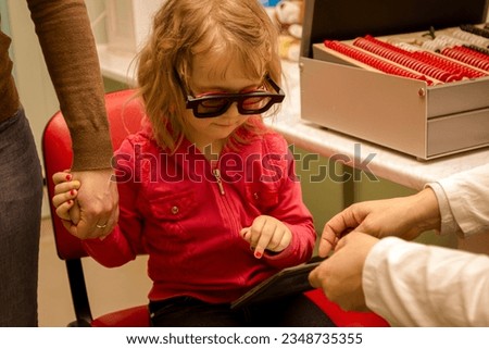 Beautiful little girl holds mom's hand, wears big black stereoscopic 3D glasses for checking stereo vision, eyesight exam, stereotest.