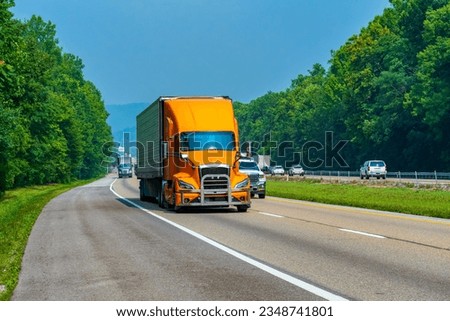 Horizontal shot of an orange eighteen wheeler in traffic on an interstate highway. Royalty-Free Stock Photo #2348741801
