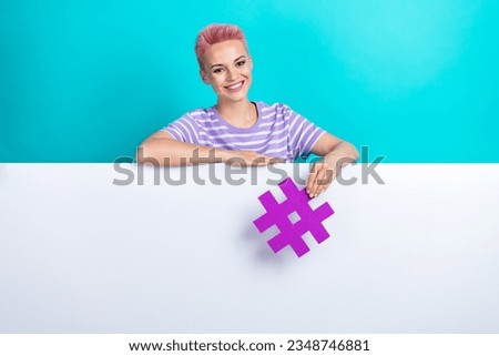 Photo of pretty cheerful girl stand behind empty space ad blank hand hold hashtag symbol isolated on teal color background