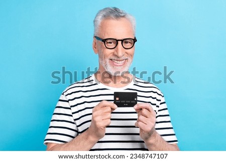 Photo portrait of handsome grandad specs hold credit card money ecommerce dressed stylish striped clothes isolated on blue color background