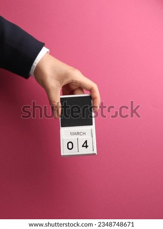 March 4 wooden block calendar in male hand on pink background
