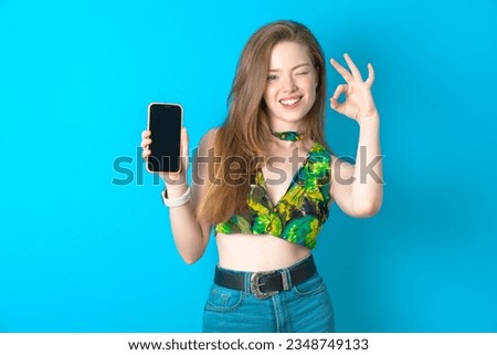 Young woman wearing floral T-shirt holding in hands cell showing ok-sign